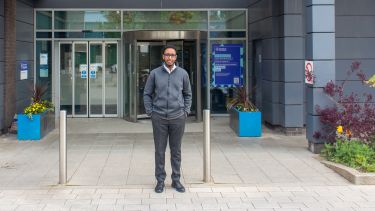 A man is stood in front of the University of Sheffield Medical School