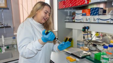 A young woman with blonde hair and a lab coat tests samples in the lab.