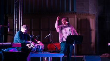 Two performers on stage singing and playing tabla 