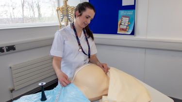 Emma wearing a student midwife uniform practising on a manikin measuring an expecting mother's bump