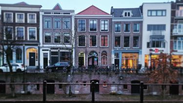 Six tall terraced houses shown from across a canal in Utrecht. Railings in the foreground.