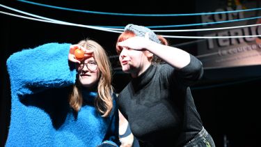 Two young women sheltering their eyes looking into an audience 