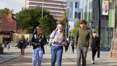 Three students smiling and laughing as they walk through campus 