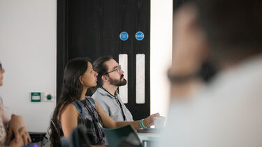 two people sat at table looking up at screen
