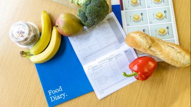 Selection of healthy foods on a wooden table with a book marked "Food diary."
