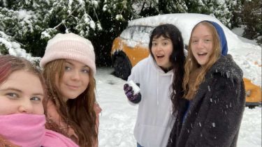 Four students posing in the snow with scarves and hats