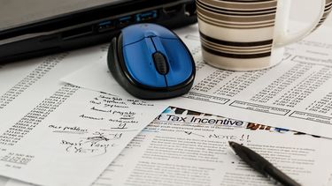 Papers with numbers with a pen, computer mouse, laptop and a mug.