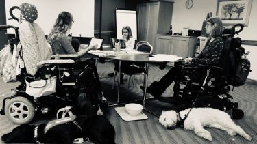 Three disabled researchers and two assistance dogs sat at an office table