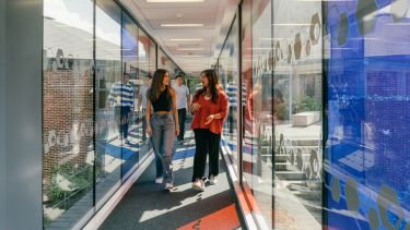 Students walking down a glass walled corridor.