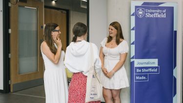 Three women stood next to a sign that reads 'The university of Sheffield. Journalism - be Sheffield Made'.