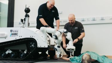 Two researchers from the University of Sheffield making adjustments to the MediTel robot while it triages a model patient