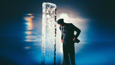 A photograph of composer Erland Cooper next to a vertical ice sculpture, taken by photographer Alex Kozobolis