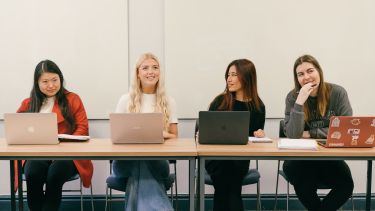 Students sitting on a table with laptops, engaged in a seminar.