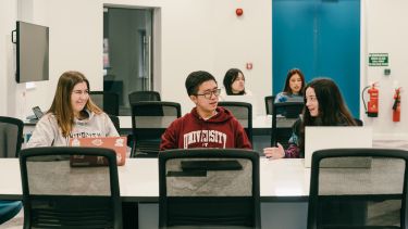 Students sitting on a table with laptops chatting in a seminar room 