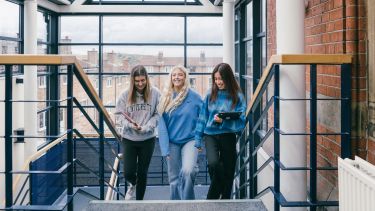Three postgraduate students walking up the staircase of Bartolomé House