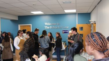 A group of visitors enjoying food and talking about the lecture they have just seen. in the foyer outside the moot court. 