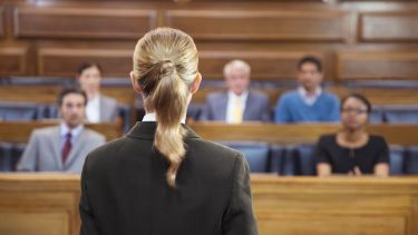 An image of a woman stood in front of a jury in a courtroom.