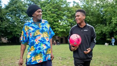 Image of older person with a teenager playing football and smiling