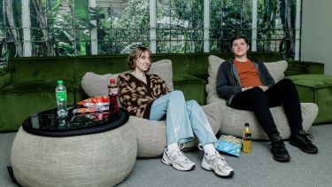 Two people sat on beanbags in a room looking towards a screen, there are drinks and snacks on the table