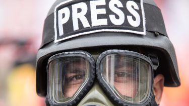 A man wearing a gas mask and a helmet marked 'PRESS'.