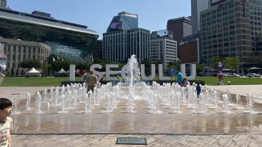 A wide shot of a fountain in front of a Seoul sign