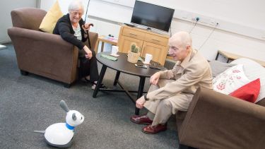 Two elderly people looking at a small robotic dog.
