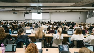 A large lecture theatre filled with students sitting in front of laptops.