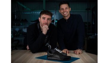 Fyous co-founders Thomas Bloomfield and Joshua Shires lean on a table which has one of their medical footwear shoes on.
