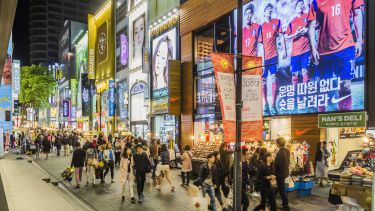 People walking down a busy shopping street in Seoul, South Korea, at night surrounded by neon signs