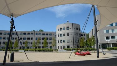 Photograph taken from beneath an awning, showing concrete university buildings against a blue sky
