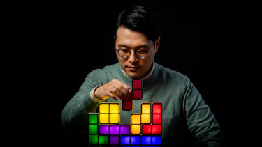 A man with multicolour Tetris-style building blocks against a black background.