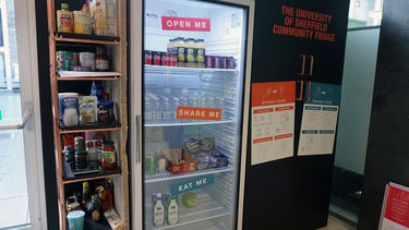 A large fridge full of food and drink items with a large shelving unit next to it full of ambient goods