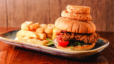 Stacked chicken burger with onion rings and chips