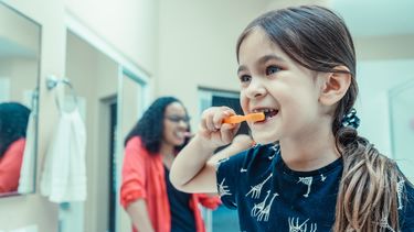 A child holding an orange tooth brush and brushing their teeth