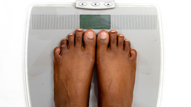 A pair of feet standing closely together on weighing scales