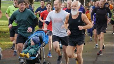 Group of people young and old running, including one person pushing a pram.
