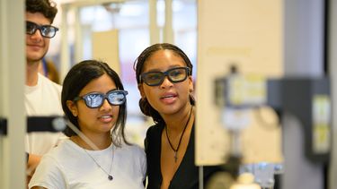 Three students (two females and one male) wearing protective eye gear in front of a stress fracture kit