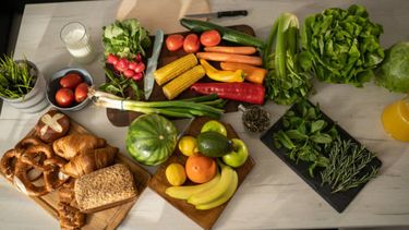 A table with lots fruit, veg and bread.