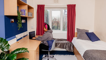 A girl sat at a desk working on a laptop in a bedroom