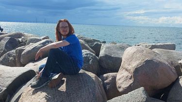 Young person sat on rocks with a long bridge in the background