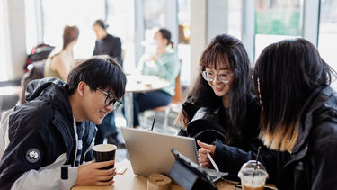 An image of students socialising and looking at a laptop 