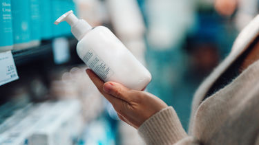 A close up of a woman holding a plastic bottle containing hand cream in a supermarket