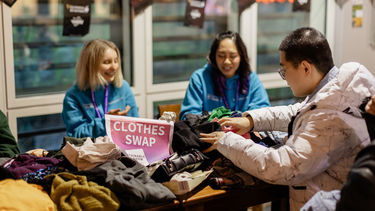 Two Mentors sat at a table filled with clothes while a man looks through the items