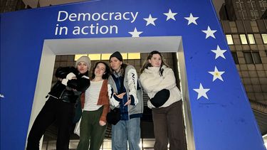four students standing in a giant frame with EU flag and text Democracy in action