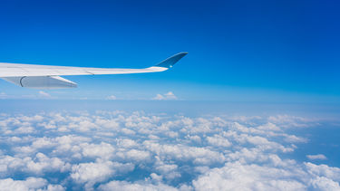 The view of a plane's wing against a blue sky with clouds as seen from a passenger window