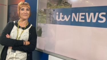 A woman with short red hair standing next to an 'ITV NEWS' sign