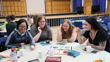 A group of girls playing board games at a table in a grand hall.