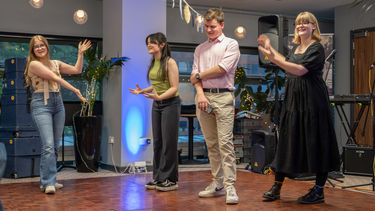 Four young people standing on a dance floor clearly delivering an informal presentation