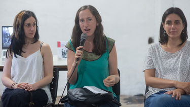 A panel of three speakers, with the person in the middle holding a microphone