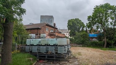 Ballast and Scaffolding in front of a red brick single storey building, trees on either side